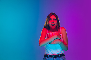 Image showing Caucasian young woman\'s portrait isolated on gradient purple-blue background in neon light, cinema, movie watching