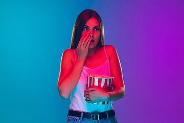 Image showing Caucasian young woman\'s portrait isolated on gradient purple-blue background in neon light, cinema, movie watching