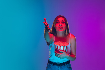 Image showing Caucasian young woman\'s portrait isolated on gradient purple-blue background in neon light, cinema, movie watching