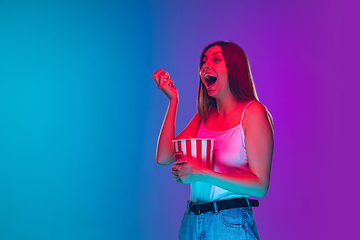 Image showing Caucasian young woman\'s portrait isolated on gradient purple-blue background in neon light, cinema, movie watching