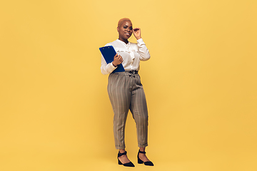 Image showing Young african-american woman in casual wear on yellow background. Bodypositive female character, plus size businesswoman