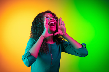 Image showing African-american young woman\'s portrait isolated on gradient yellow-green background in neon light