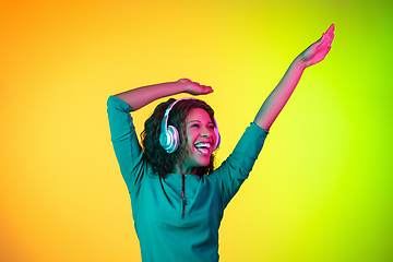 Image showing African-american young woman\'s portrait isolated on gradient yellow-green background in neon light