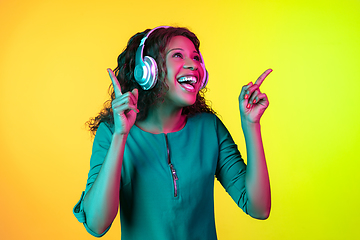 Image showing African-american young woman\'s portrait isolated on gradient yellow-green background in neon light