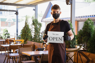 Image showing The waiter works in a restaurant in a medical mask, gloves during coronavirus pandemic