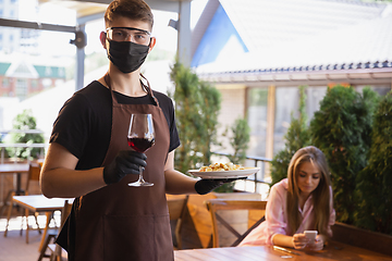 Image showing The waiter works in a restaurant in a medical mask, gloves during coronavirus pandemic