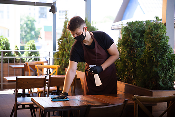 Image showing The waiter works in a restaurant in a medical mask, gloves during coronavirus pandemic