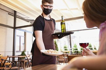 Image showing The waiter works in a restaurant in a medical mask, gloves during coronavirus pandemic