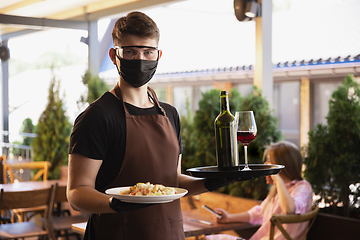 Image showing The waiter works in a restaurant in a medical mask, gloves during coronavirus pandemic