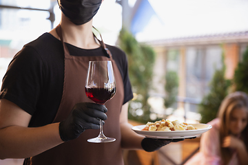 Image showing The waiter works in a restaurant in a medical mask, gloves during coronavirus pandemic