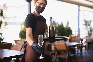 Image showing The waitress works in a restaurant in a medical mask, gloves during coronavirus pandemic