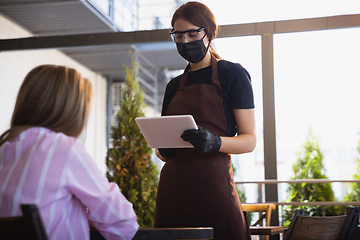 Image showing The waitress works in a restaurant in a medical mask, gloves during coronavirus pandemic