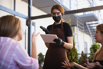 Image showing The waitress works in a restaurant in a medical mask, gloves during coronavirus pandemic