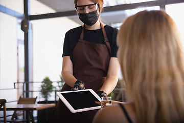 Image showing The waitress works in a restaurant in a medical mask, gloves during coronavirus pandemic