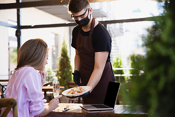 Image showing The waiter works in a restaurant in a medical mask, gloves during coronavirus pandemic