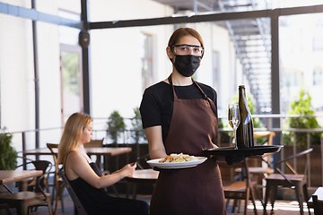 Image showing The waitress works in a restaurant in a medical mask, gloves during coronavirus pandemic