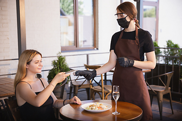 Image showing The waitress works in a restaurant in a medical mask, gloves during coronavirus pandemic