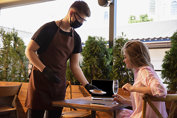 Image showing The waiter works in a restaurant in a medical mask, gloves during coronavirus pandemic