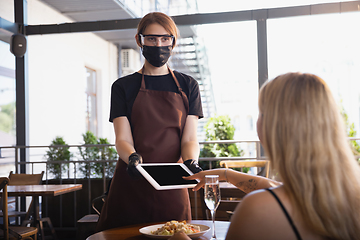 Image showing The waitress works in a restaurant in a medical mask, gloves during coronavirus pandemic