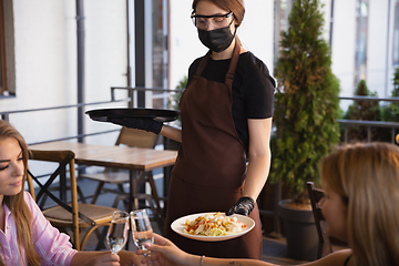 Image showing The waitress works in a restaurant in a medical mask, gloves during coronavirus pandemic