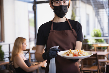 Image showing The waitress works in a restaurant in a medical mask, gloves during coronavirus pandemic