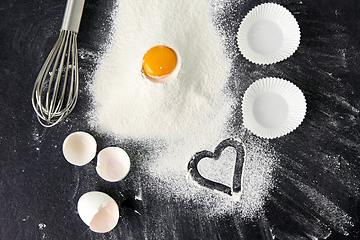 Image showing flour, egg, whisk and paper baking molds on table