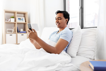 Image showing happy indian man with smartphone in bed at home
