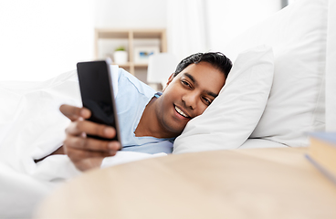 Image showing happy indian man with smartphone in bed at home