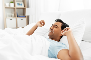 Image showing happy indian man stretching in bed at home