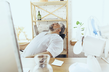 Image showing Businessman, manager in office with computer and fan cooling off, feeling hot, flushed