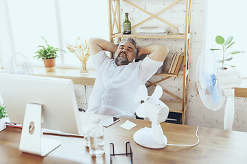 Image showing Businessman, manager in office with computer and fan cooling off, feeling hot, flushed