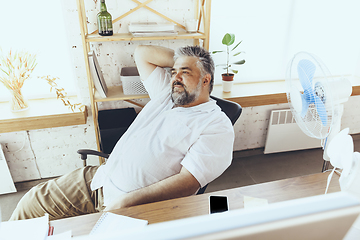 Image showing Businessman, manager in office with computer and fan cooling off, feeling hot, flushed