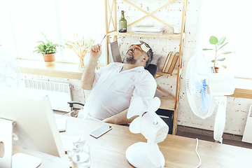 Image showing Businessman, manager in office with computer and fan cooling off, feeling hot, flushed