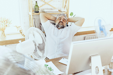 Image showing Businessman, manager in office with computer and fan cooling off, feeling hot, flushed