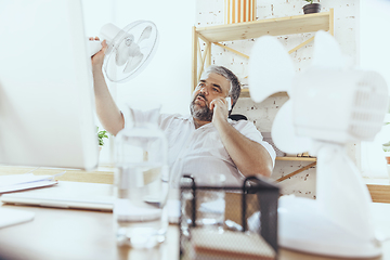 Image showing Businessman, manager in office with computer and fan cooling off, feeling hot, flushed