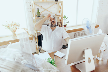 Image showing Businessman, manager in office with computer and fan cooling off, feeling hot, flushed