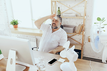 Image showing Businessman, manager in office with computer and fan cooling off, feeling hot, flushed