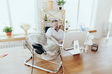 Image showing Businessman, manager in office with computer and fan cooling off, feeling hot, flushed