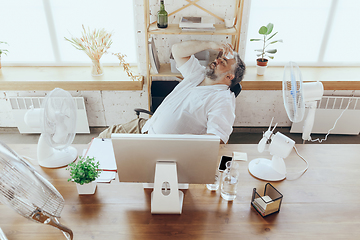 Image showing Businessman, manager in office with computer and fan cooling off, feeling hot, flushed