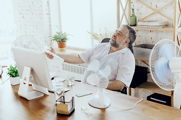 Image showing Businessman, manager in office with computer and fan cooling off, feeling hot, flushed