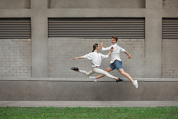 Image showing Jumping young couple in front of buildings, on the run in jump high