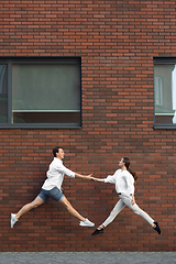 Image showing Jumping young couple in front of buildings, on the run in jump high