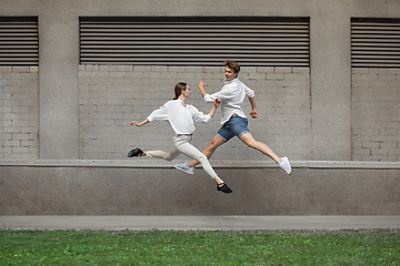 Image showing Jumping young couple in front of buildings, on the run in jump high