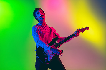 Image showing Young caucasian musician, guitarist playing on gradient background in neon light. Concept of music, hobby, festival