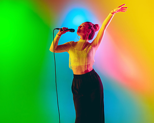 Image showing Young caucasian musician playing, singing on gradient background in neon light. Concept of music, hobby, festival