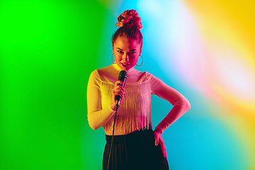 Image showing Young caucasian musician playing, singing on gradient background in neon light. Concept of music, hobby, festival