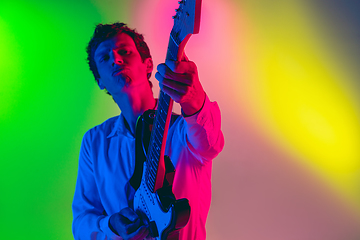 Image showing Young caucasian musician, guitarist playing on gradient background in neon light. Concept of music, hobby, festival