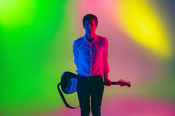 Image showing Young caucasian musician, guitarist playing on gradient background in neon light. Concept of music, hobby, festival