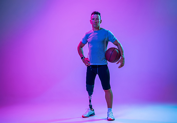 Image showing Athlete with disabilities or amputee isolated on gradient studio background. Professional male basketball player with leg prosthesis training and practicing in studio.