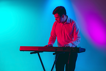 Image showing Young caucasian musician, keyboardist playing on gradient background in neon light. Concept of music, hobby, festival